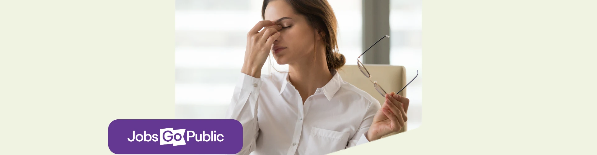 Frustrated female employee is holding her glasses in one hand and pinching her nose with her eyes closed