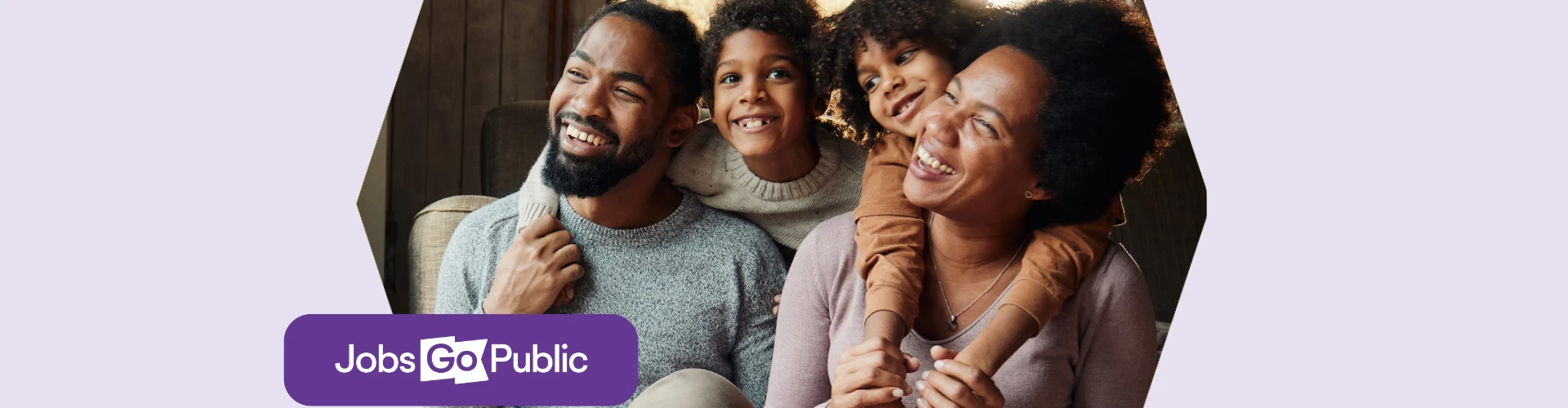 A mother and father are sat on the floor enjoying time off work, smiling with their two sons leaning over their shoulders