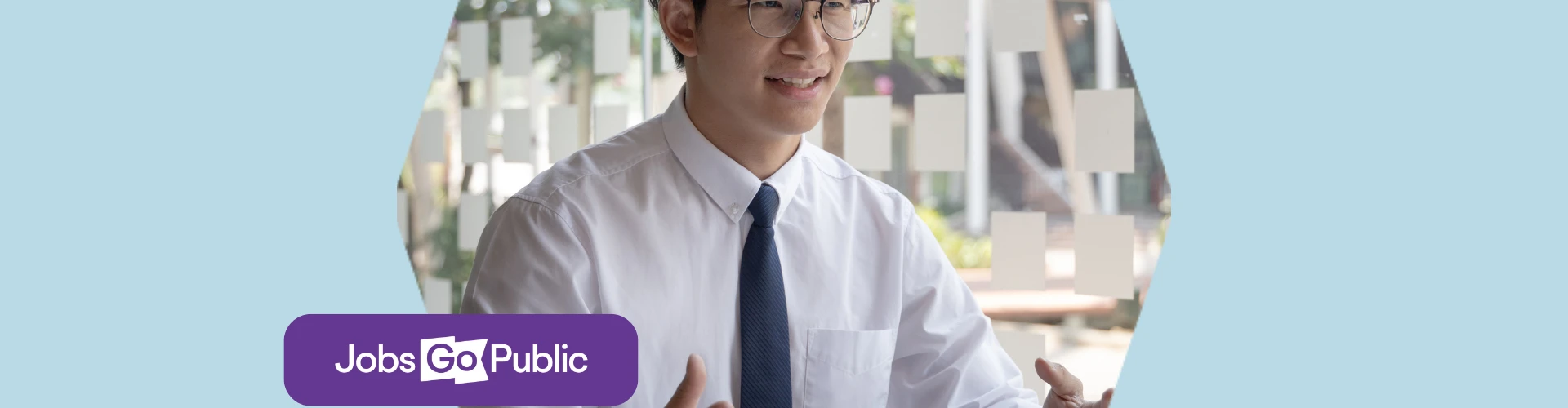A man in glasses, a shirt, and tie is sat at a desk speaking animatedly to a hiring manager off screen