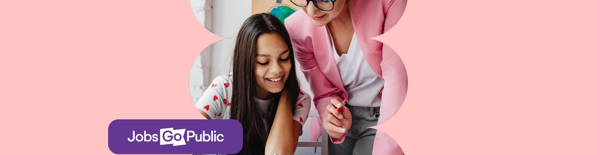 A female public sector teacher in a state school is leaning over a desk helping a female student with her work
