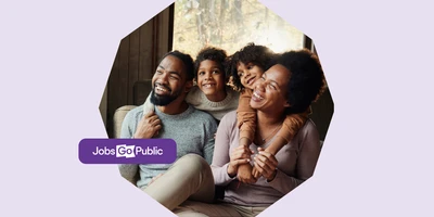 A mother and father are sat on the floor enjoying time off work, smiling with their two sons leaning over their shoulders