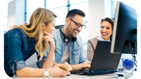 A team of IT professionals are gathered round a laptop smiling and having a discussion