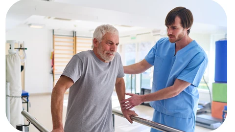 A physiotherapist in blue scrubs is working with a male patient in his 60s who is walking with the aid of bars