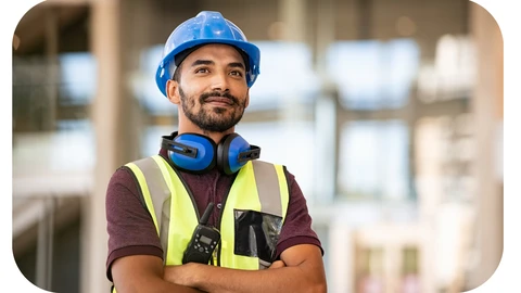 A health and safety professional is shown wearing a high visibility vest, blue hard hat, and has ear protectors sitting round his neck.
