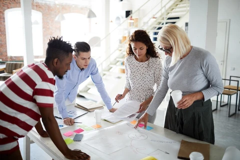 A project team of four is standing around a table looking at a planning mind map.